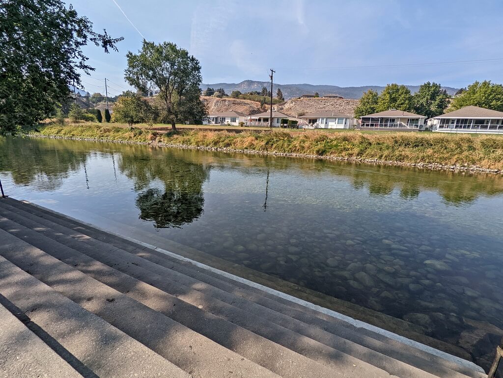 Steps leading down into calm Penticton Channel, with housing visible on the other side