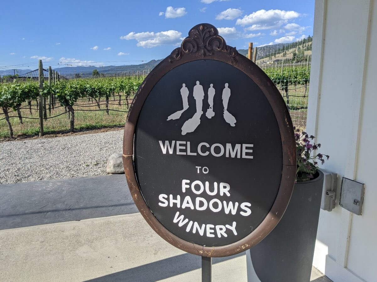 Close up of 'Welcome to Four Shadows Winery sign' on old mirror, with vineyards visible in the background