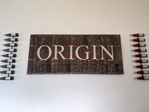 "Origin" wall sign on the wall with wine bottles row on each side