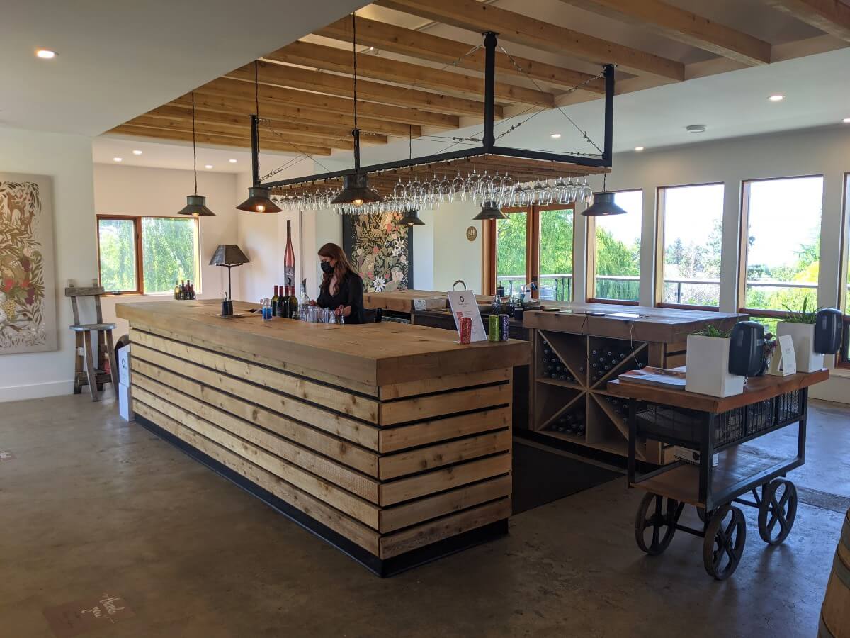 Side view of two sided wooden wine tasting bar at Three Sisters Winery, with wine glasses hanging from ceiling