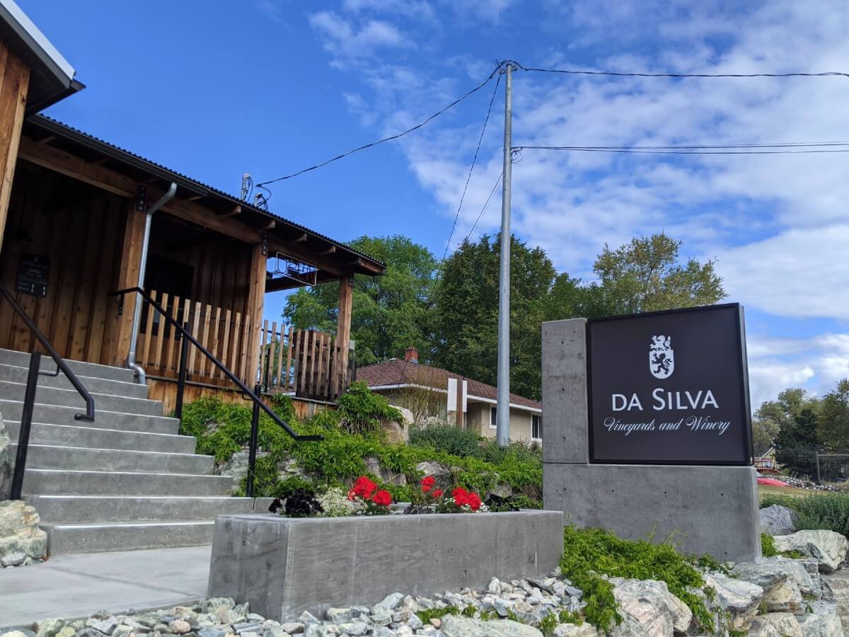 Front view of Da Silva Vineyards and Winery, with concrete steps leading up to wooden building, with concrete sign on right with winery name and logo