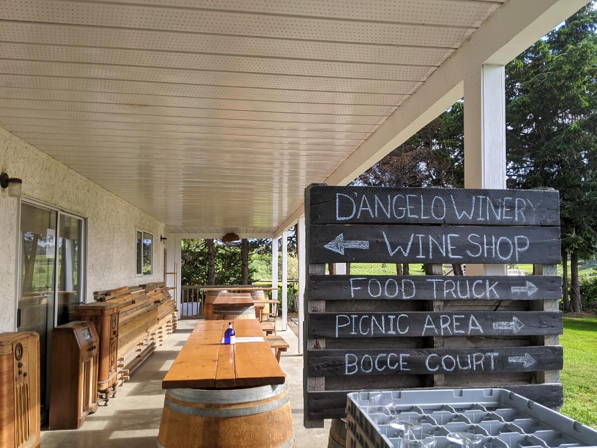 Undercover tasting area at D'Angelo Winery without three bar areas visible, and chalkboard on right with arrows pointing to wine shop, food truck, picnic area and bocce court