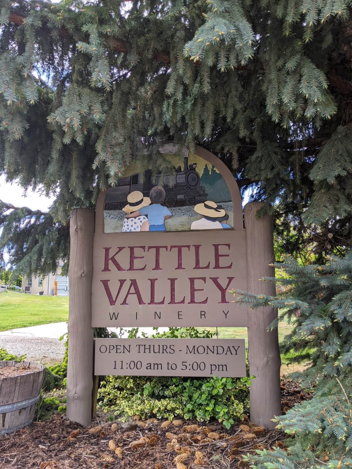 Kettle Valley Winery wooden sign with logo, picture of family and train and opening times beneath