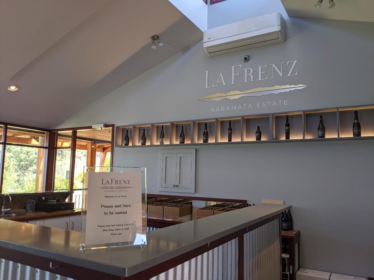 View of La Frenz tasting room with C shaped white counter, white walls, La Frenz logo and mid wall shelving with wine bottles