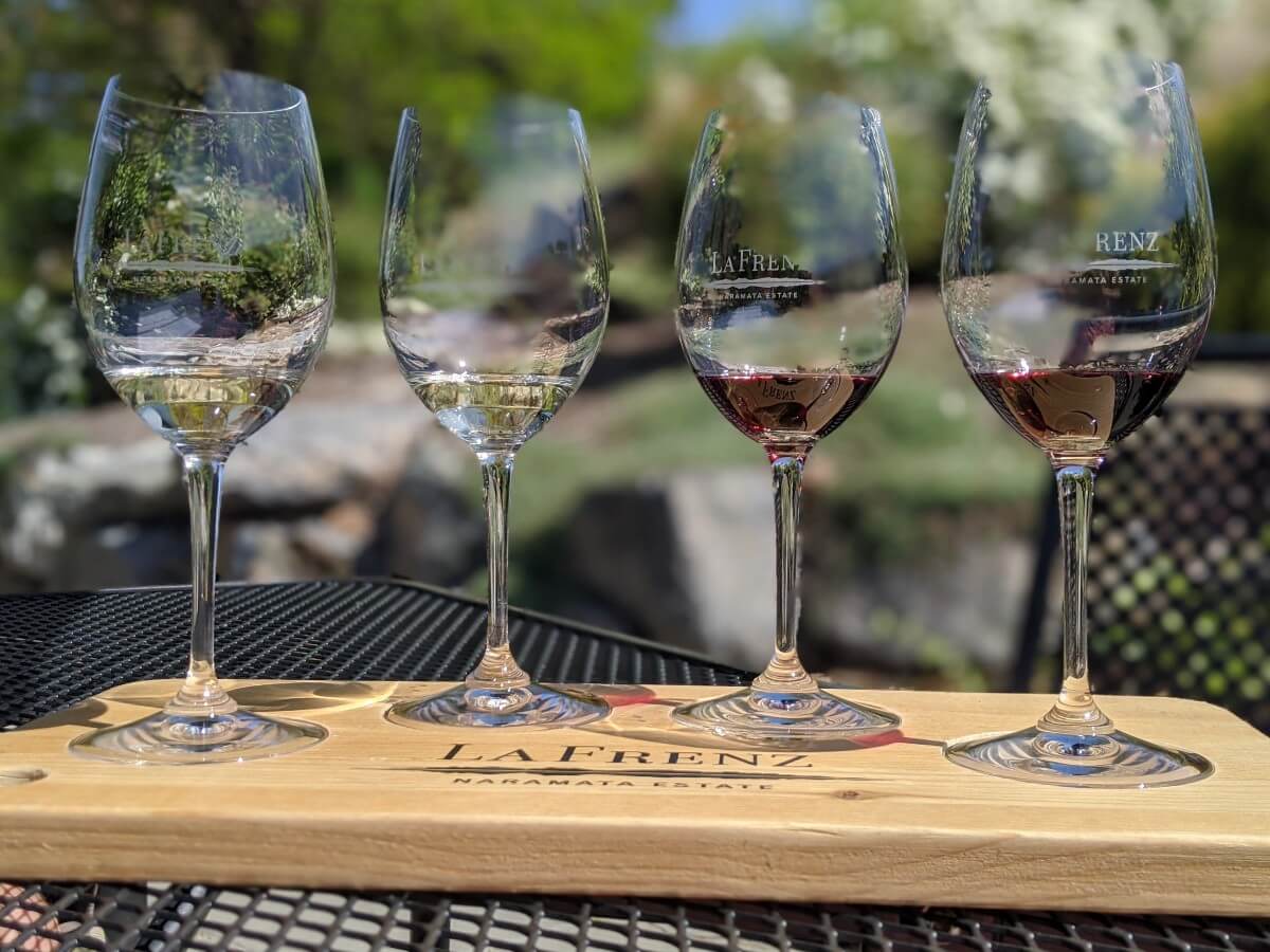 Front view of four wine glasses at La Frenz Winery, set atop wooden flight board on patio table