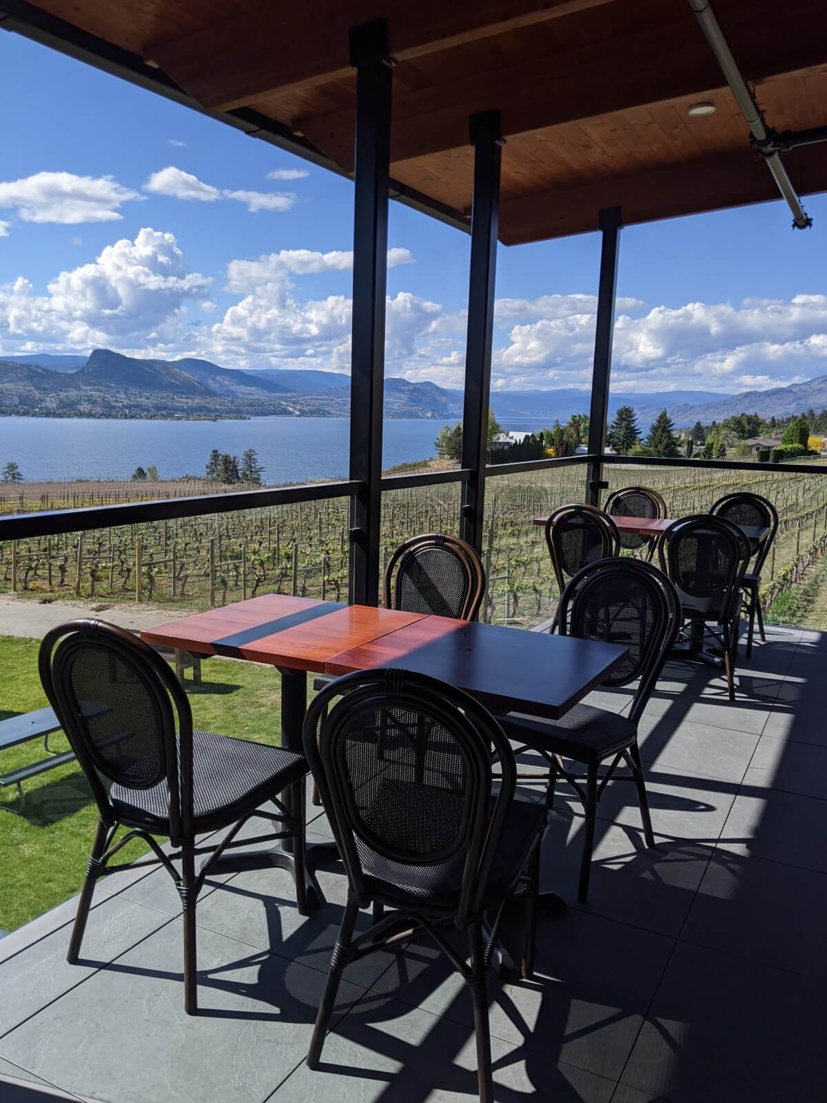 Looking across covered tasting room patio, with two tables (each with four seats), in front of vineyard and Okanagan Lake views