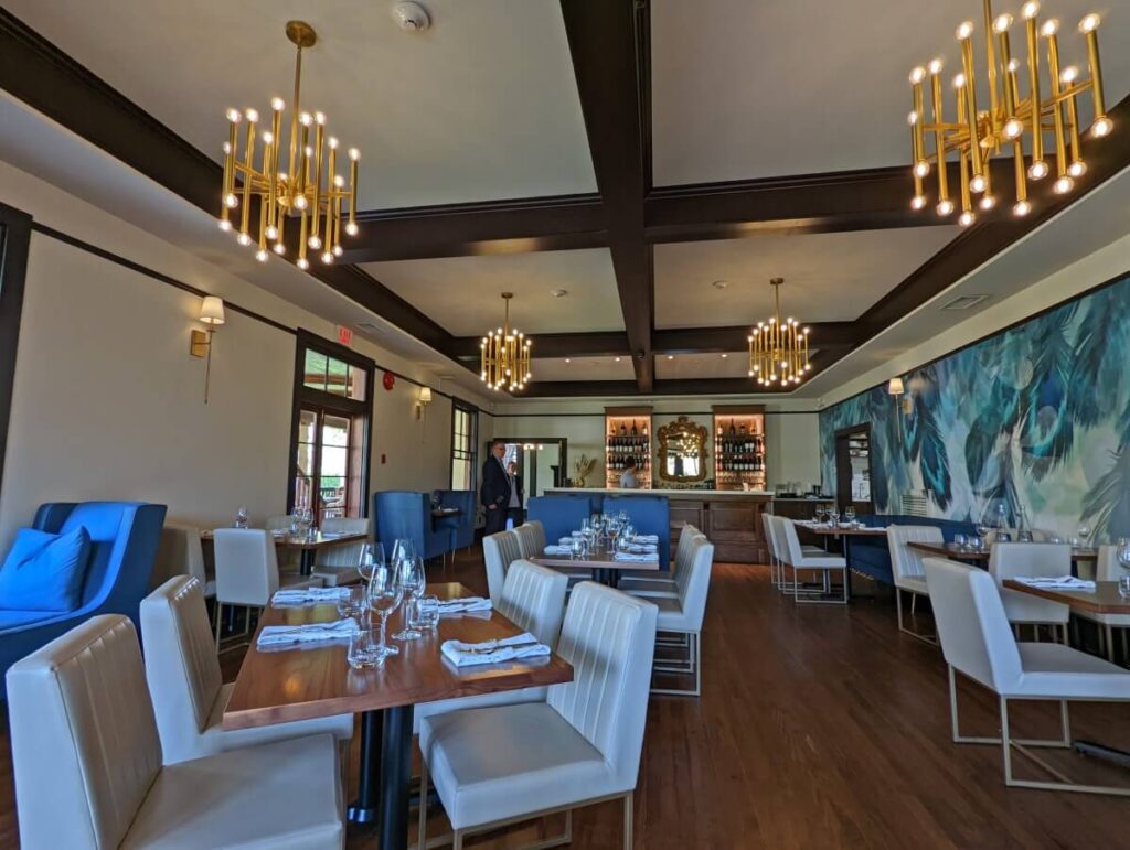Naramata Inn dining room with original 100+ year old floors, white chairs and simple chandeliers. There is blue artwork on the right