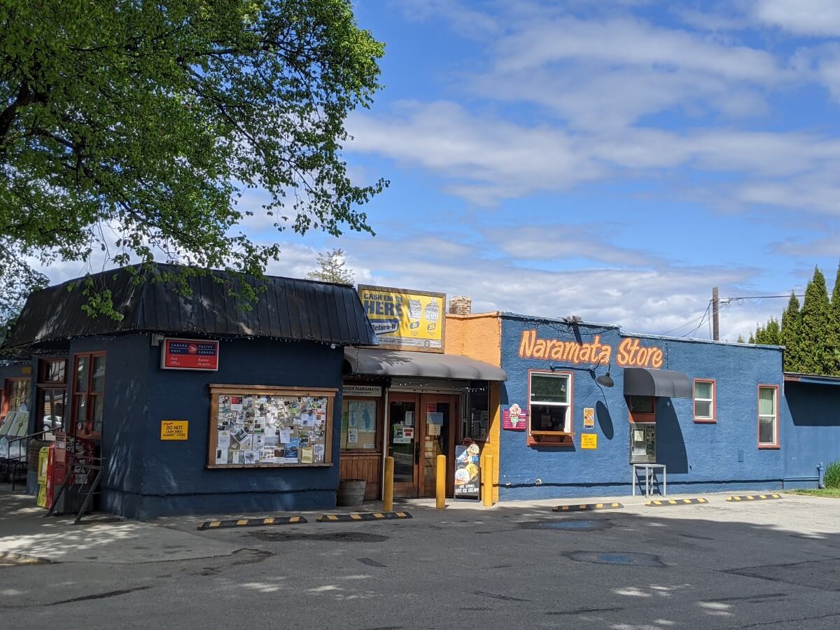 Front view of single story blue Naramata Store building and outside parking. 