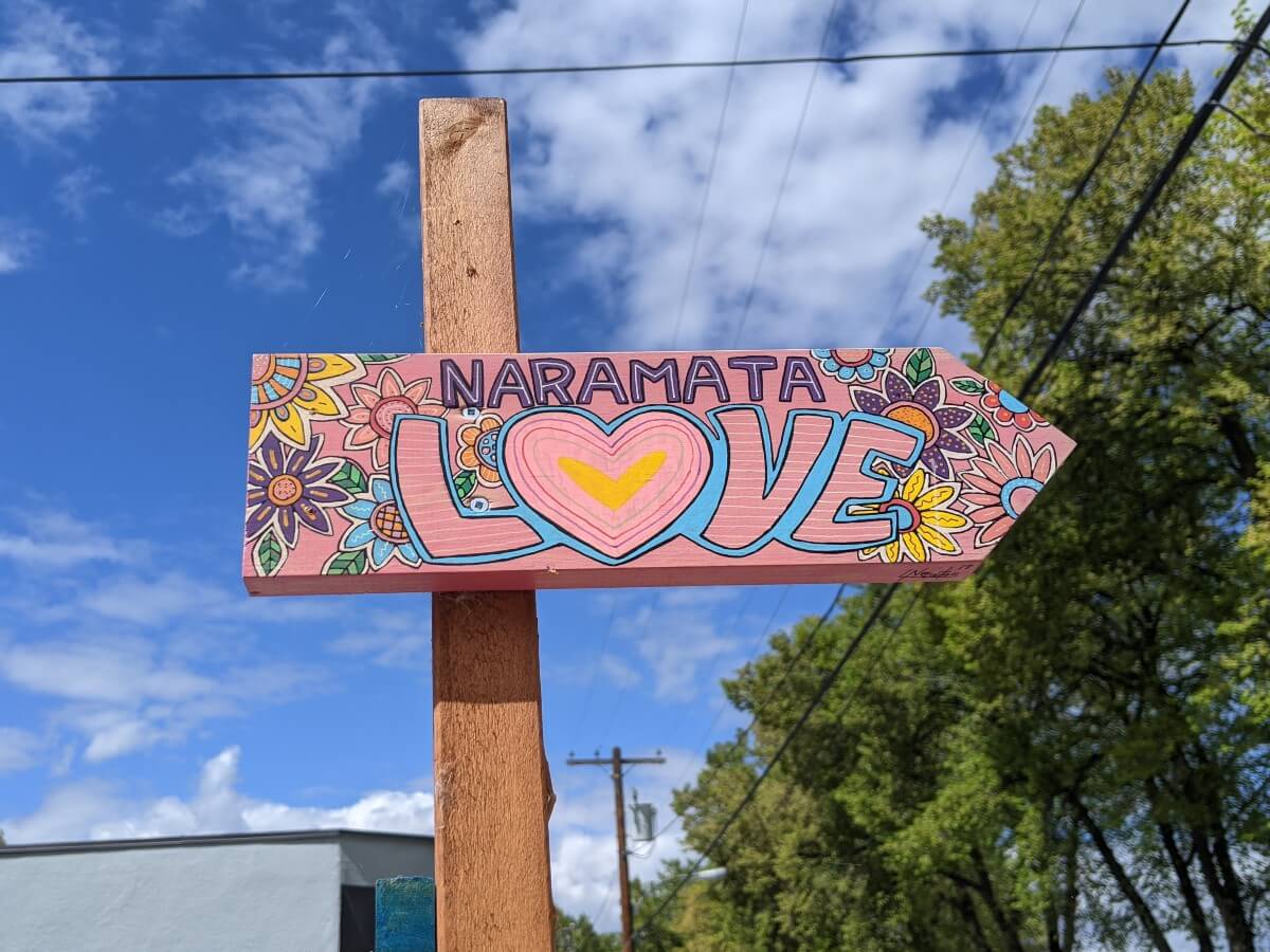 Close up of handpainted sign, painted in pink with 'Naramata Love' text on it, surrounded by flowers