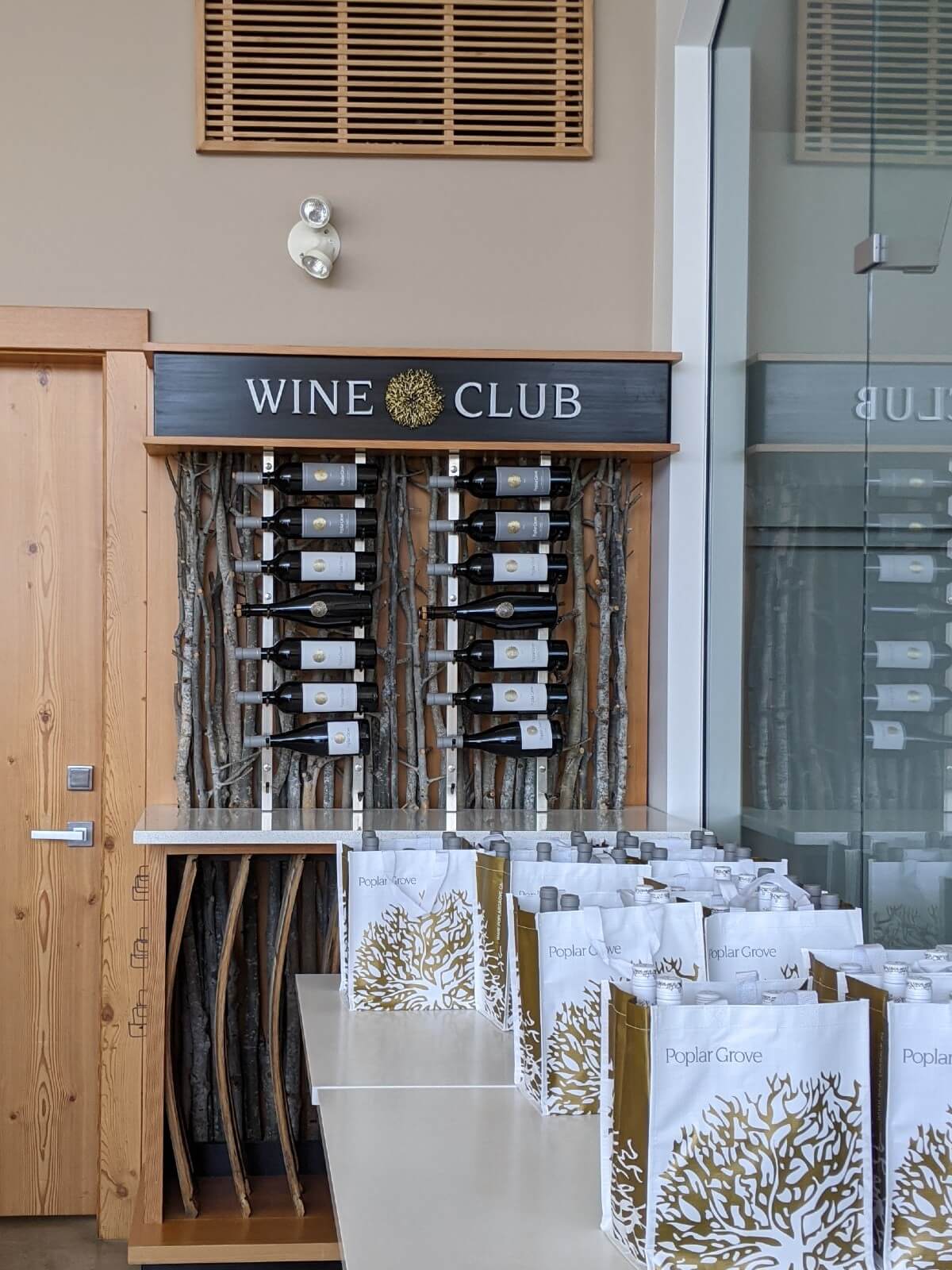 Front view of Wine Club stand at Poplar Grove winery, with display of wine bottles with Poplar Grove gift bags on table in foreground