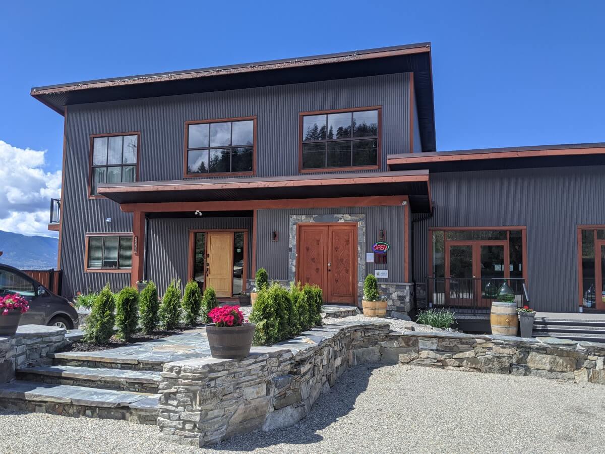 Two story grey coloured building (Wesbert Winery), with steps leading to double front door. There is a second wooden door to the left