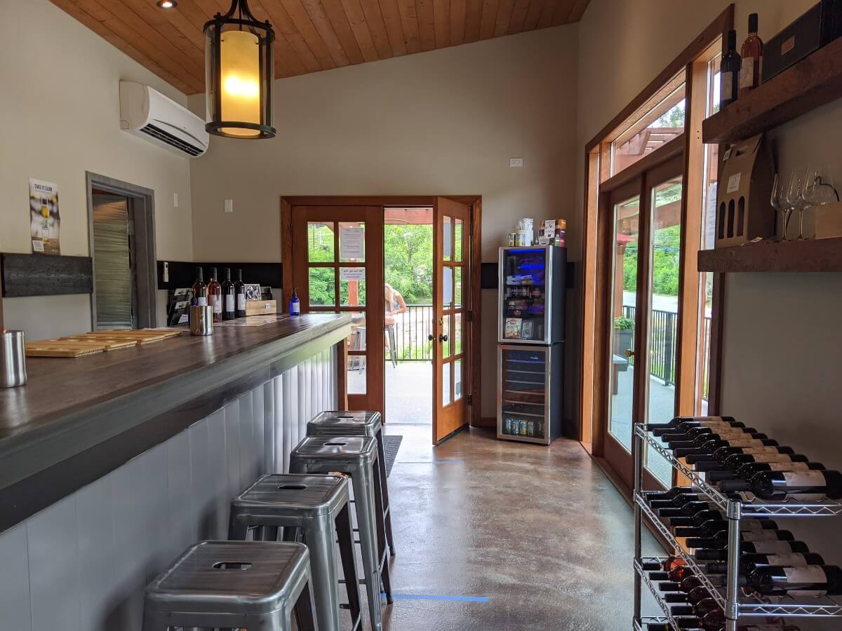 Side view of Wesbert Winery tasting room with silver bar on left, wine shelving on right and doors leading out to patio at the back