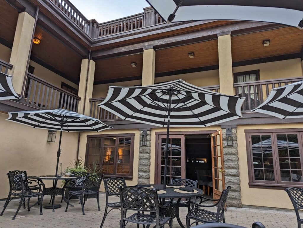 Brick patio at Eliza Wine Bar with stripey black and white umbrellas and metal patio chairs and tables, in front of Naramata Inn