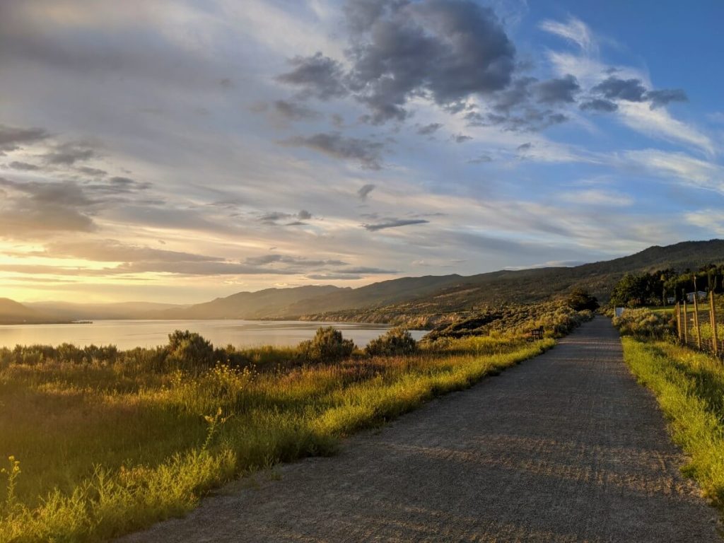 Looking ahead to gravel KVR Trail with sun setting to left, behind Okanagan Lake