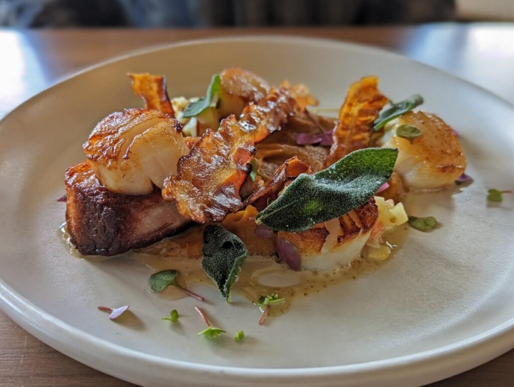 Close up of bacon and scallop dish on white plate at the Naramata Inn