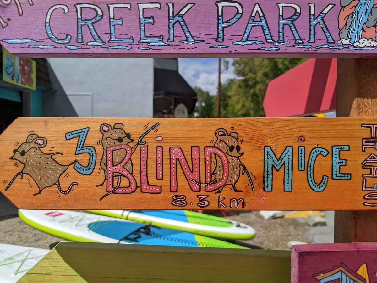 Close up of 3 Blind Mice sign, featuring the name and distance (8.3km) of trail decorated with cartoon images of mice wearing dark glasses and carrying canes. 