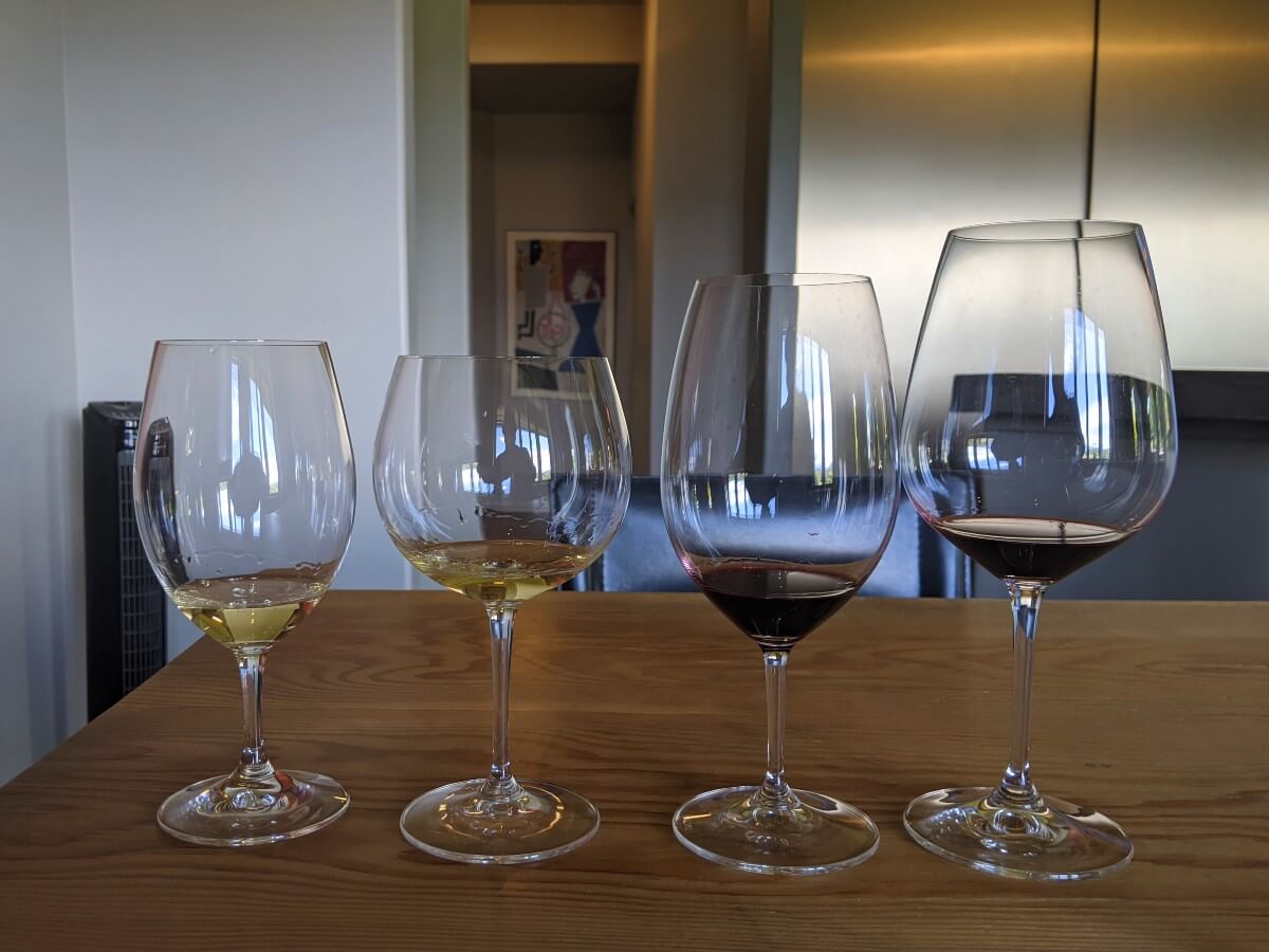 Four differently shaped wine glasses on wooden table at Laughing Stock Vineyards, two with red wine, two with red wine