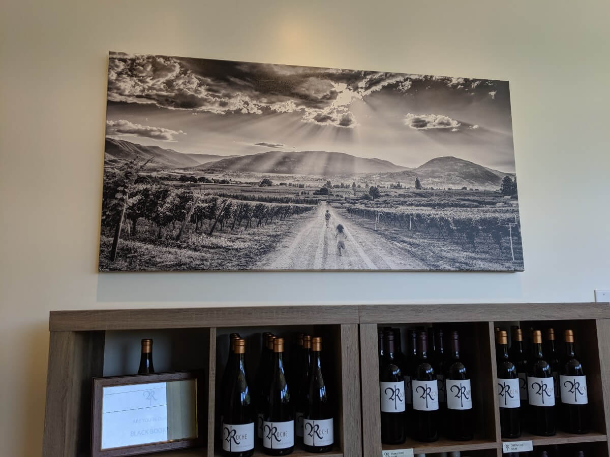 Tasting room view with shelves of wine bottles, with a black and white photography of vineyards above at Roche Wines