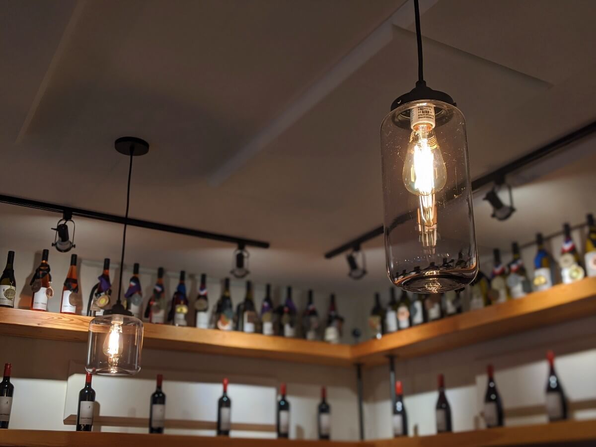 Close up of vintage lighting in Tightrope Winery tasting room, with wine bottles on shelving in background