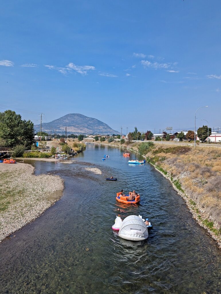 Bridge view of large beach floaties on Penticton Channel, with mountain scenery in background