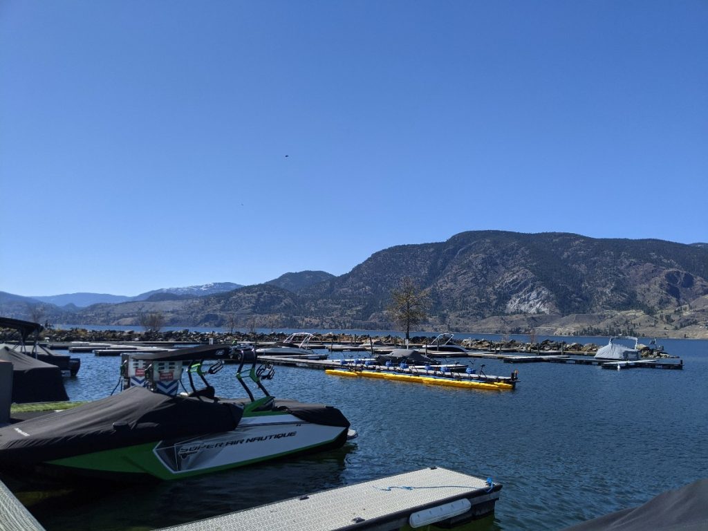 View of Skaha lake and marina with a few boats docked on pontoons with large hills in the background.