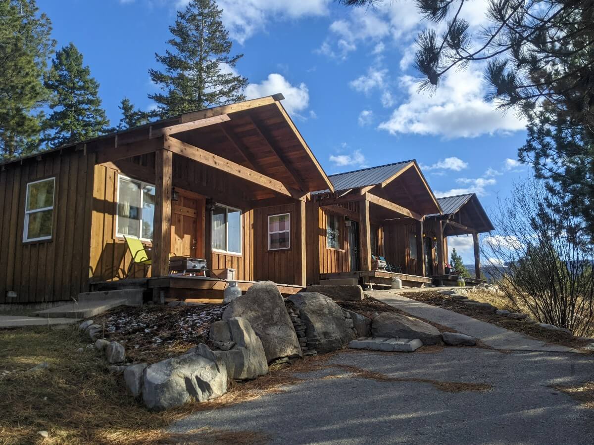 Three wooden cabins sit side by side at Lose Moose, each with small front patio featuring BBQ and seating