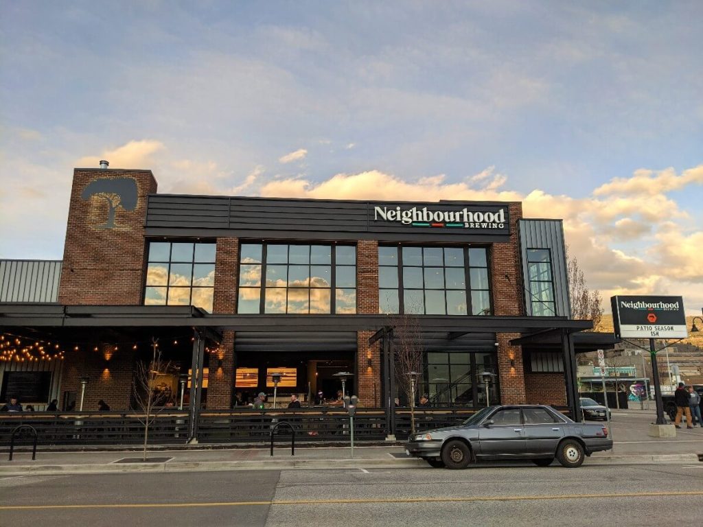 Side view of brick Neighbourhood Brewing building, with large wraparound patio (with heaters) and large windows on second floor