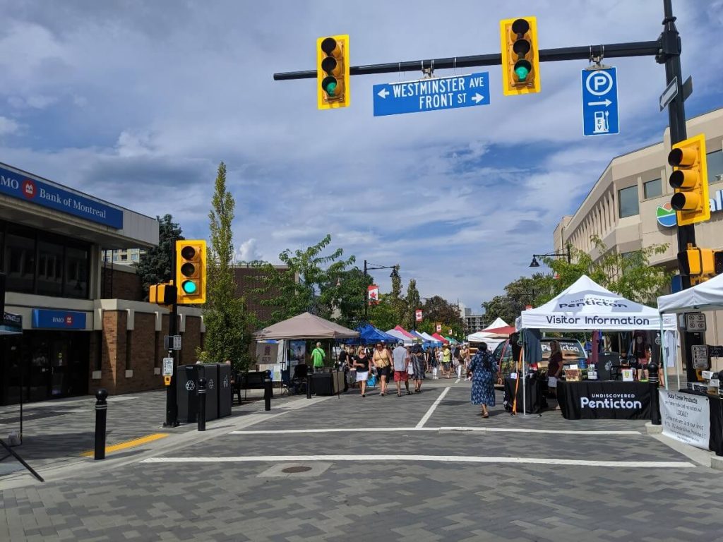 View of people walking on the road, in between tent kiosk at the Penticton Farmers Market.