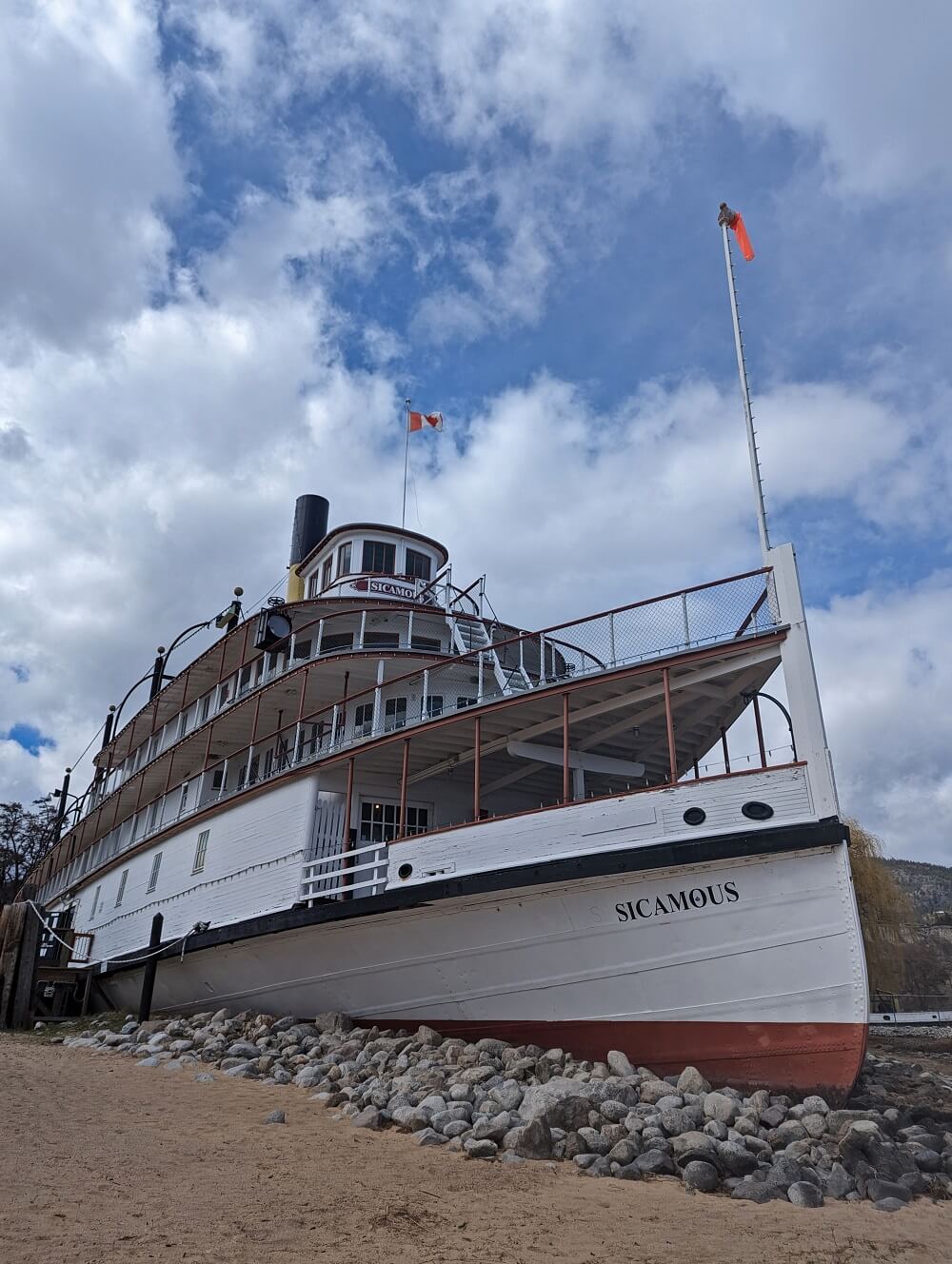 Looking up at four level wooden SS Sicamous sternwheeler ship, sitting on golden Okanagan Beach in Penticton. The boat's name is visible on the side