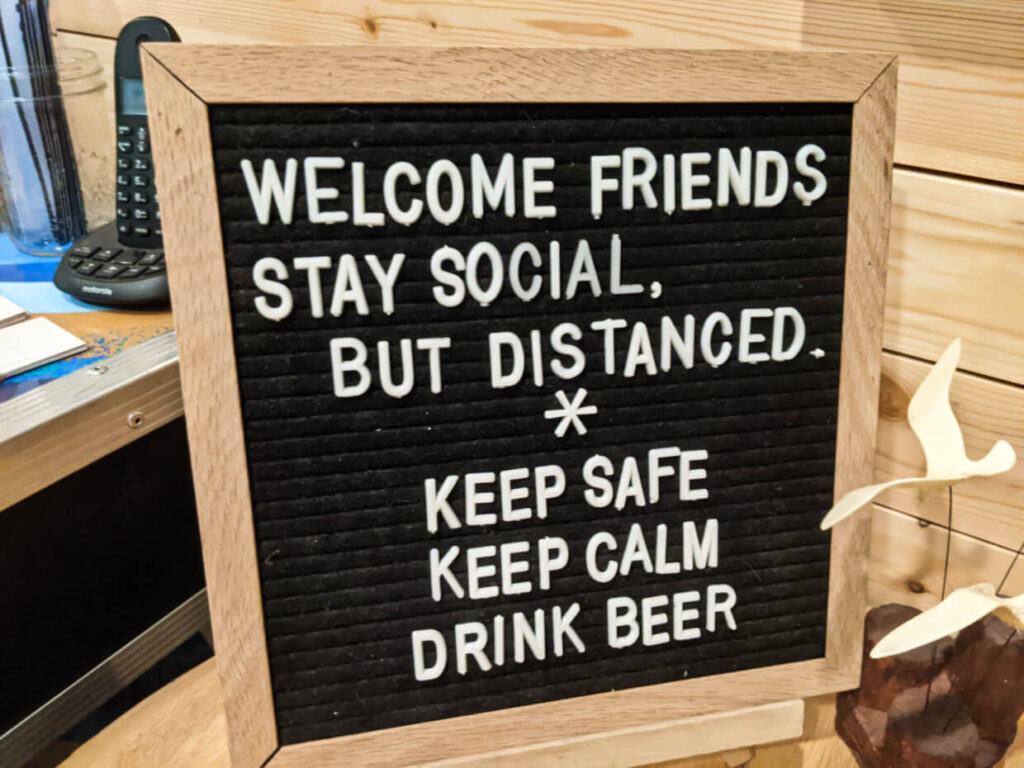 Wooden sign at Penticton restaurant with the phrasing 'Welcome Friends, Stay Social, but distanced. Keep Safe, Keep Calm, Drink Beer.'
