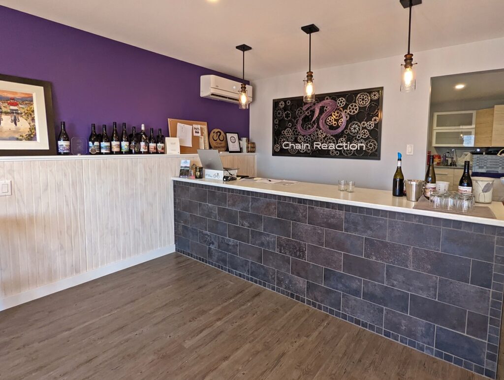 Interior view of Chain Reaction Winery tasting room with tiled bar area, purple walls and logo behind