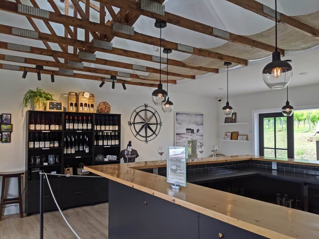 Four Shadows tasting room interior wih U-shaped wooden bar, white walls, black (wine) bookcases and hanging lights