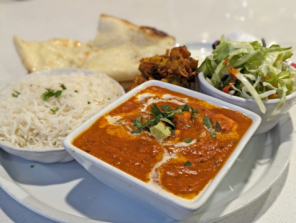 Close up shot of dinner for one plate at Penticton Indian Cuisine featuring curry dish, rice, salad, pakora and naan bread