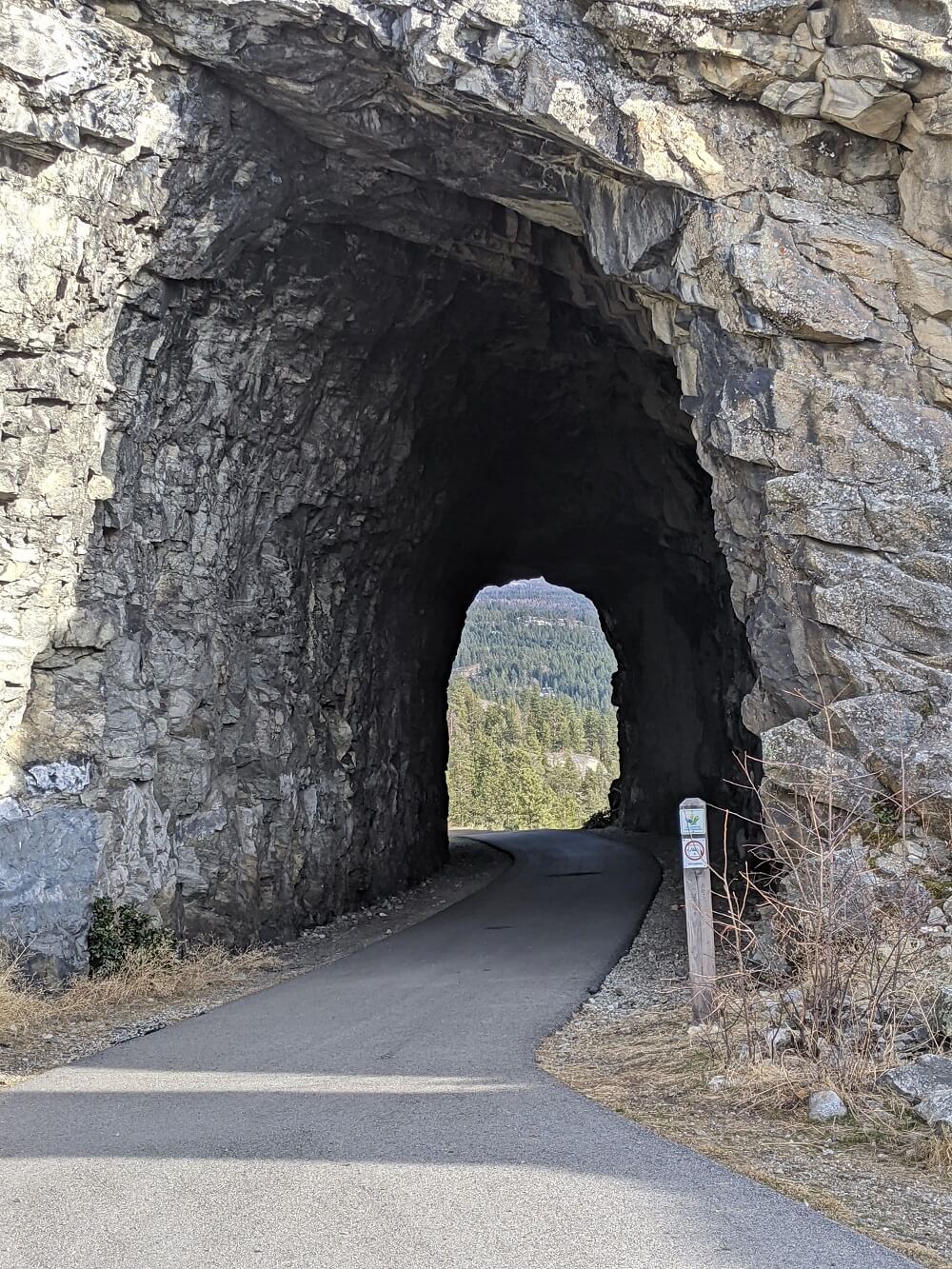 Looking through rocky blasted tunnel in Naramata, with paved path leading through centre