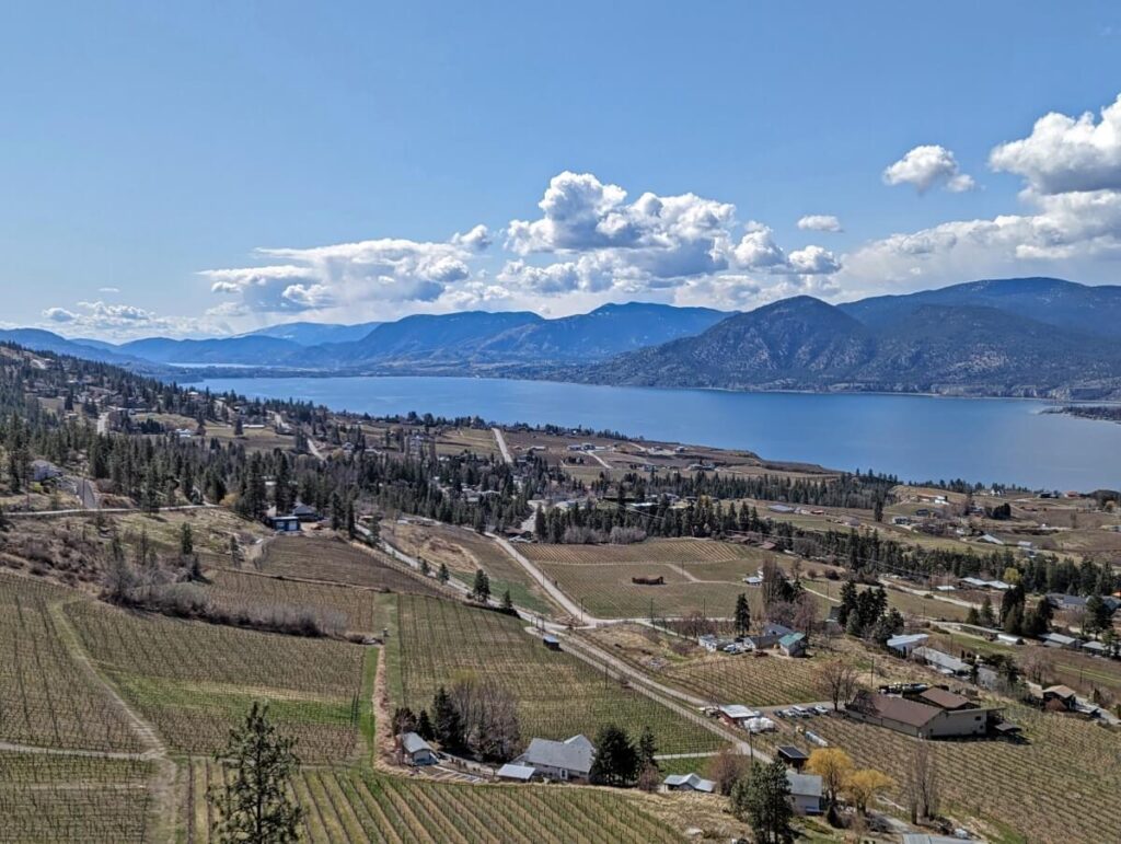 Scenic view from the Little Tunnel, looking down on vineyards next to Okanagan Lake. Forested mountains make up the backdrop on the other side of the lake