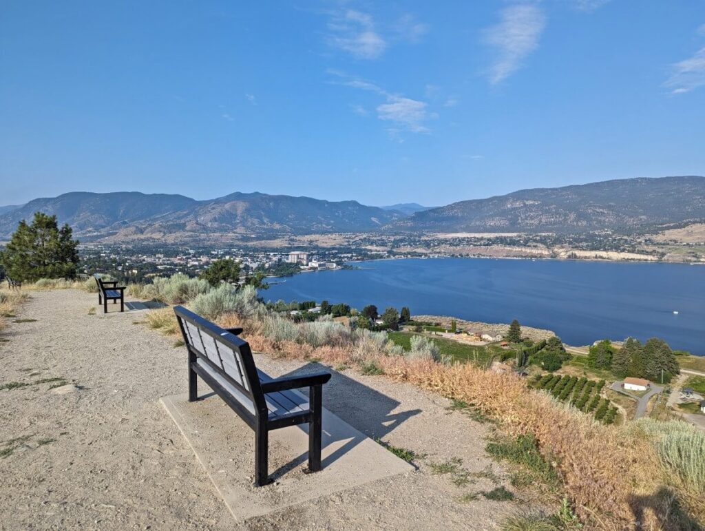 Side view of bench on Munson Mountain hike, with expansive views of Okanagan Lake and city of Penticton below, with forested hills as backdrop