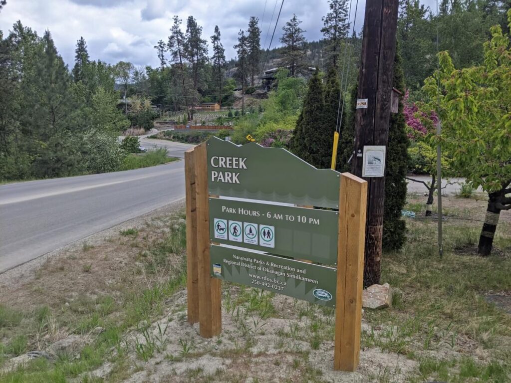 Green Creek Park sign next to Naramata Road, with park hours and Regional district information