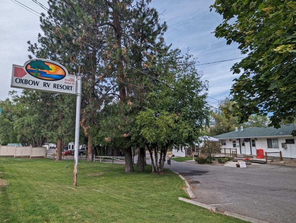 Exterior of Oxbow RV Resort, with bright signage on left and white office building on right. There are trees on a grassy area in-between