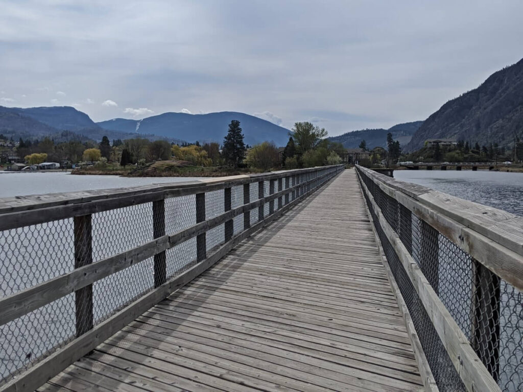 Wooden trestle bridge stretching away from camera over Okanagan Lake towards Okanagan falls with mountains in background