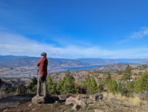 Back view of JR standing in front of panorama on Canyon View Trail, with city of Penticton and Okanagan Lake visible below