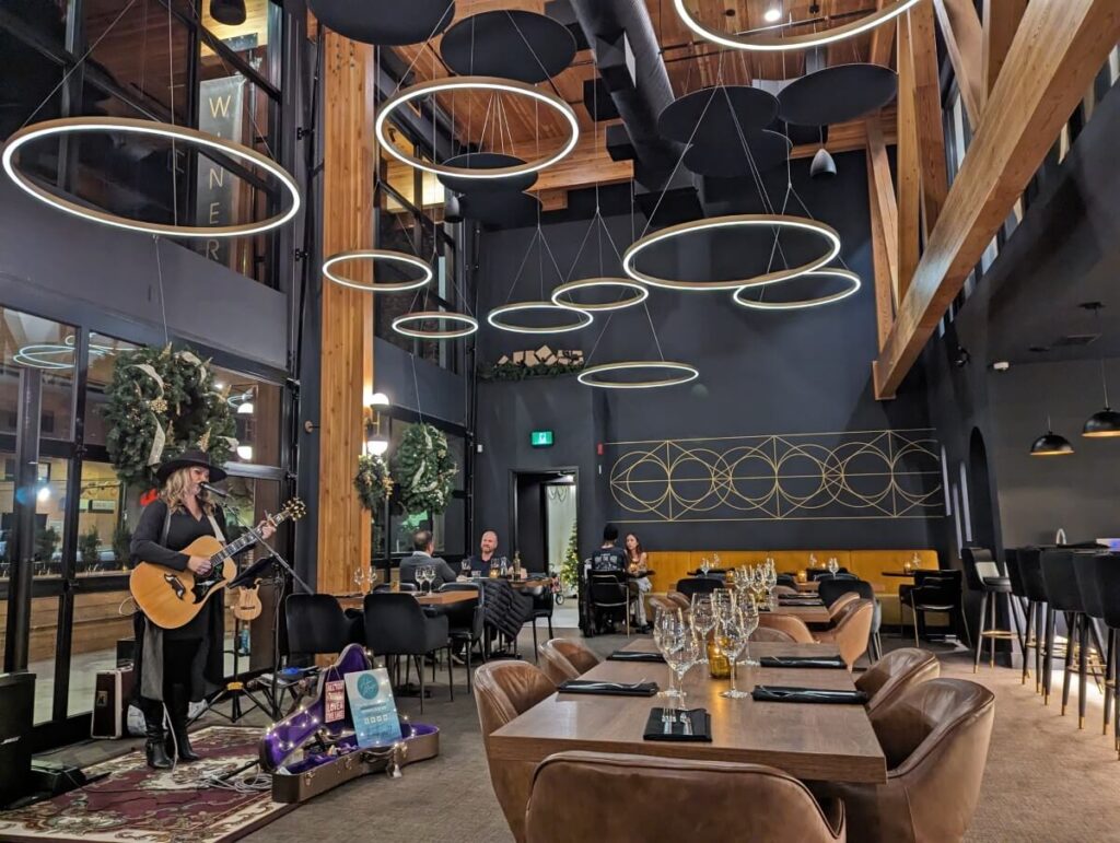 OROLO Restaurant interior with dark walls, low hanging lights, high ceilings, brown furniture. There is a singer with a guitar on left