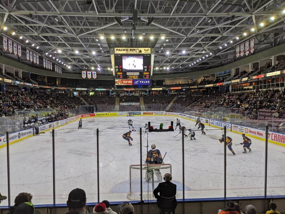 Penticton Vees hockey game, photo taken from the stands. A dozen hockey players on the ice, bright lights above, half the stands filled with crowd