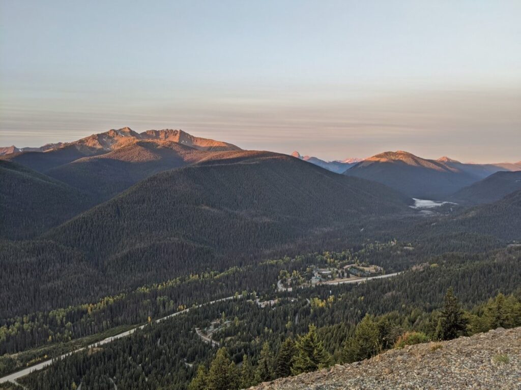 Cascade Lookout view in Manning Park, elevated viewpoint looking down on highway with forested mountains surrounding. At sunset, with light on the top of the peaks