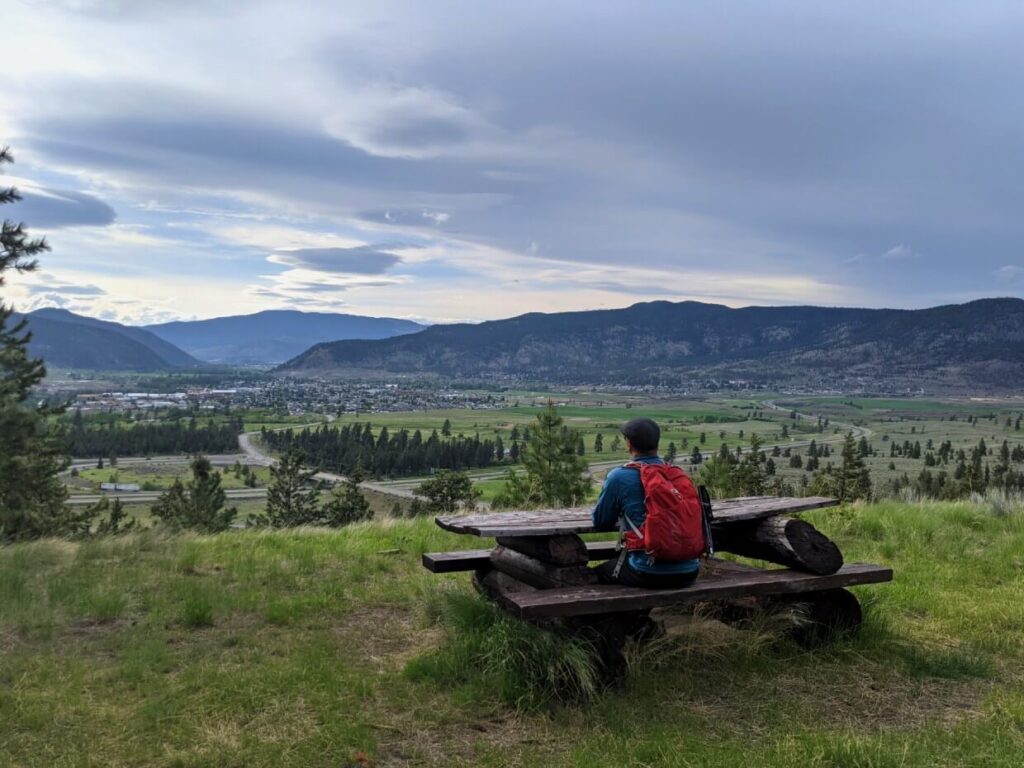 Back view of hiker sat on wooden bench in front of scenic valley view in Merritt