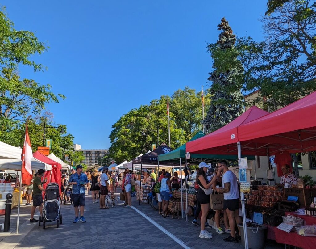 Street view of Saturday Farmers' Market in Penticton, with small stalls on both sides of the road, pedestrians walking inbetween