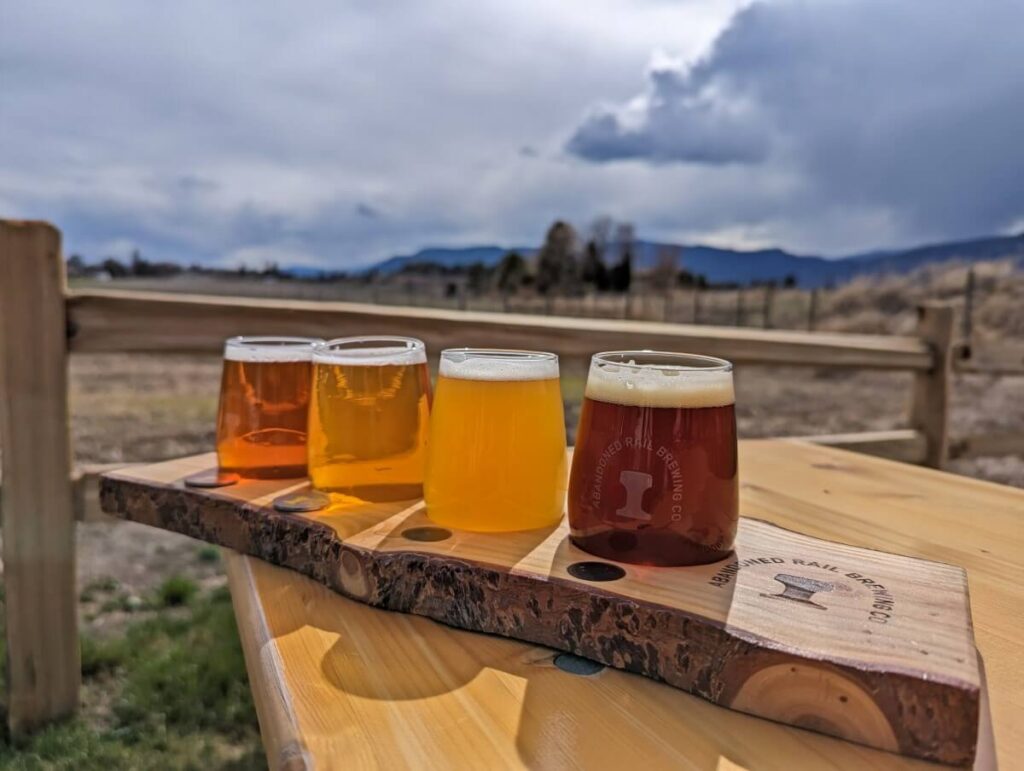 Tasting flight of four beers on wooden holder, perched on table on outside patio at Abandoned Rail Brewing