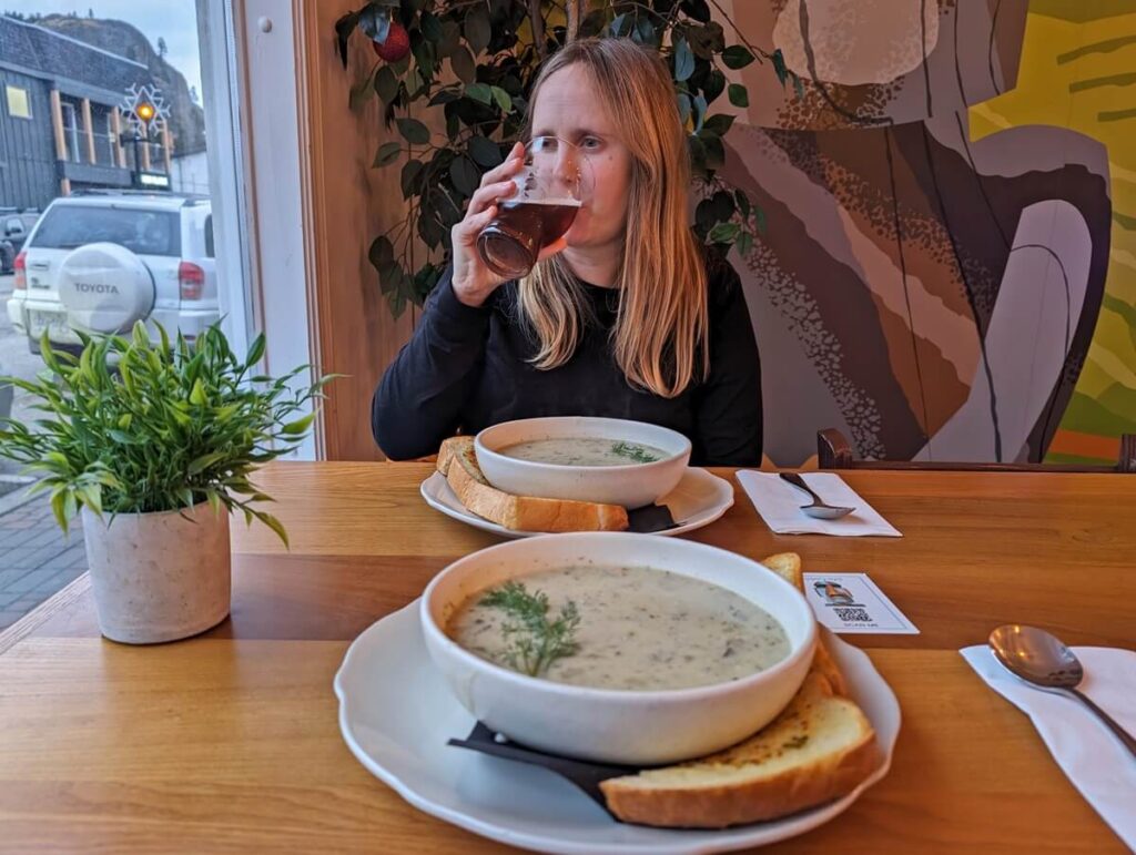 Looking across table to woman drinking beer, with two bowls of seafood chowder on the table 