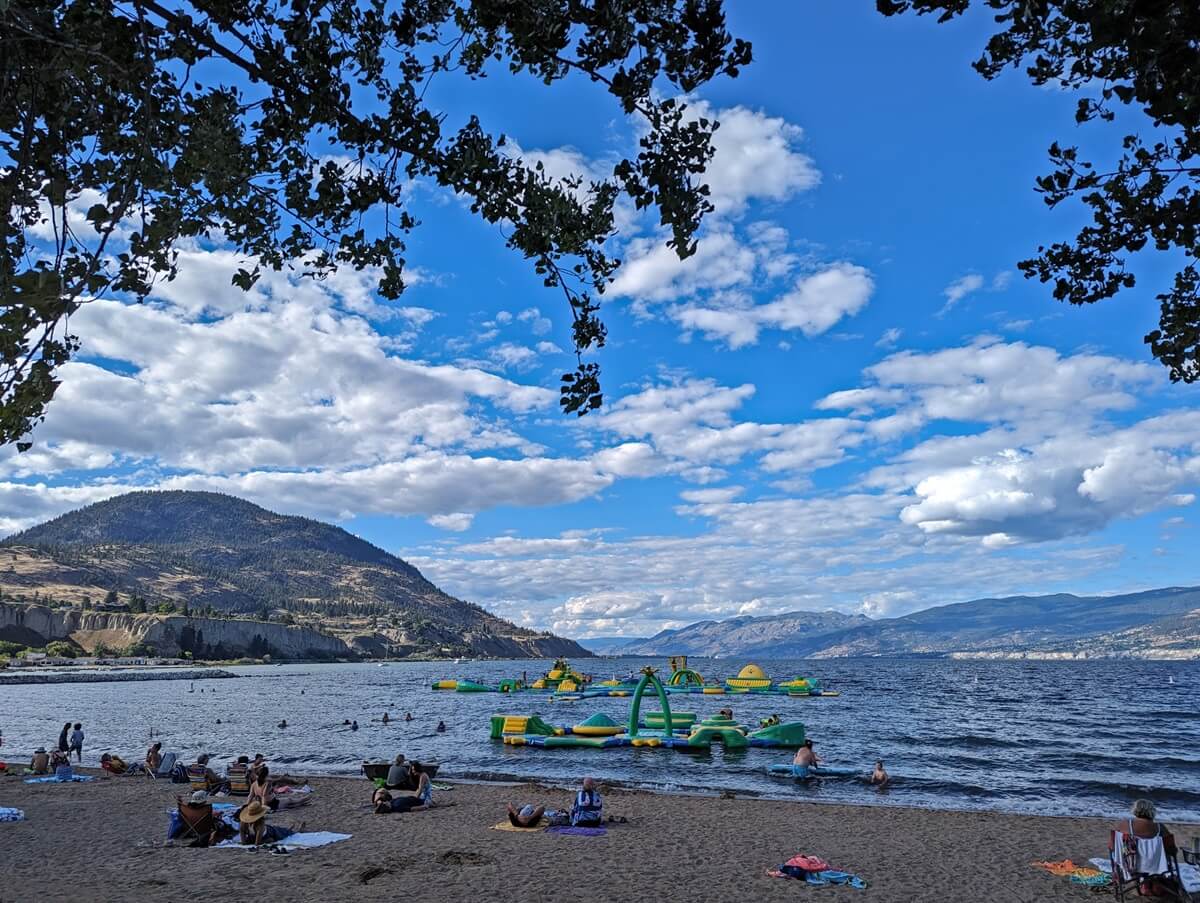 View through the trees to sandy Okanagan Lake beach and inflatable Splash BC play structure