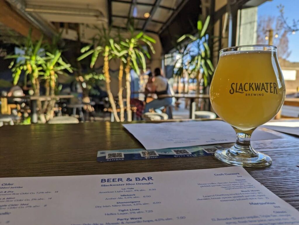 Glass of yellow coloured beer next to menu on table at Slackwater Brewing in Penticton