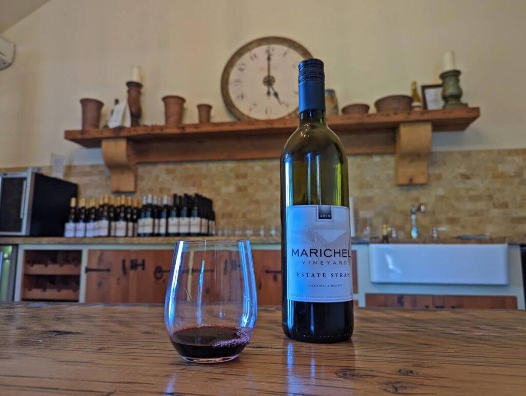 Marichel Vineyards tasting room interior with glass wine bottle and partially full red wine glass in front of farmhouse kitchen style counter